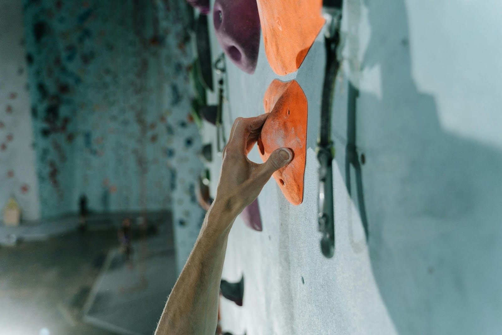 A climber's hand grasping an orange hold on a rock climbing wall, showcasing the sport's challenge and athleticism.