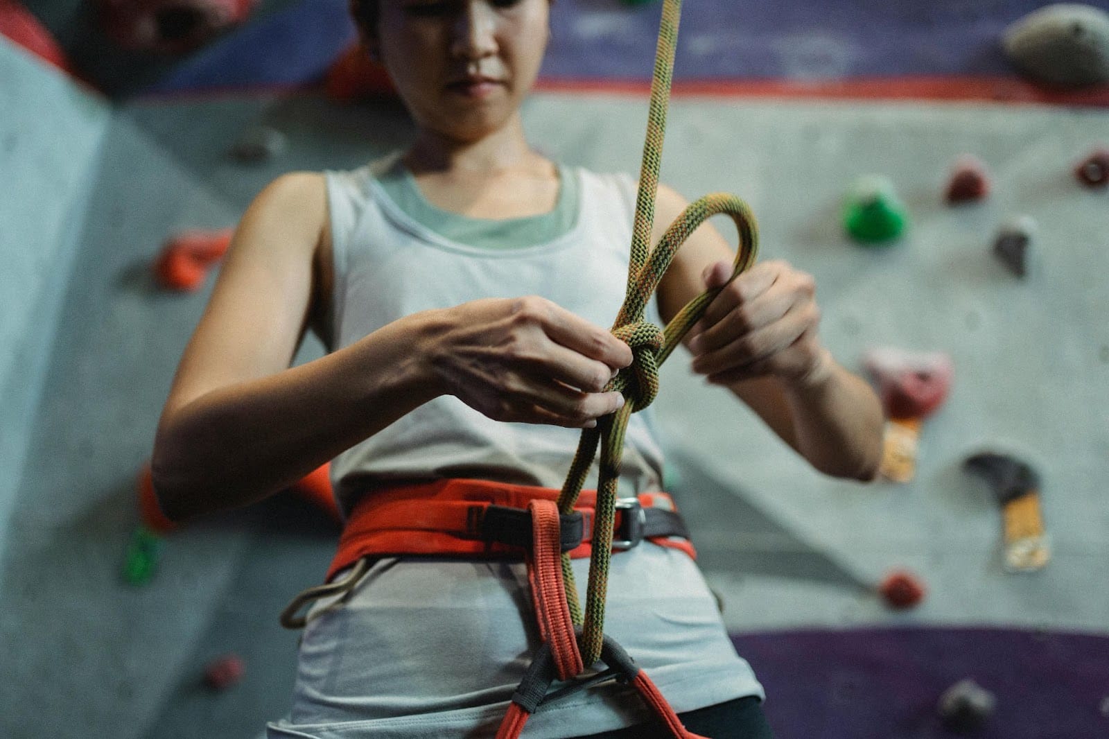 A climber carefully securing their rope harness in preparation for scaling the vibrant, textured climbing wall.