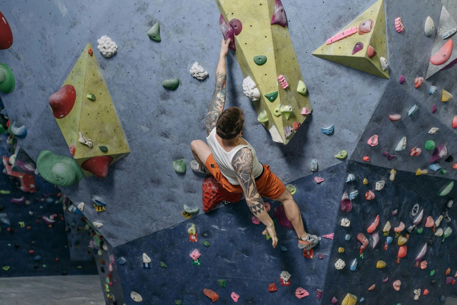 A person climbs on a vibrant, multicolored indoor rock climbing wall, grasping various shaped and textured holds in an array of bright hues.