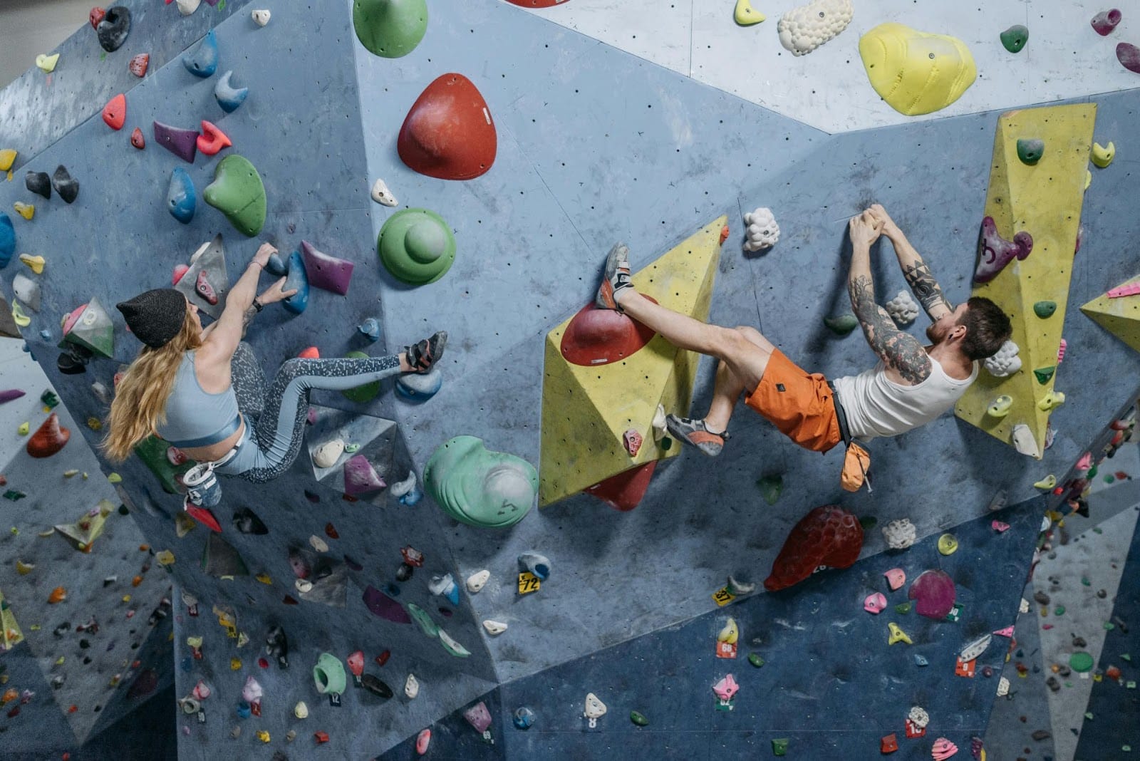 Two rock climbers scaling a tall, colorful indoor climbing wall, demonstrating the agility and technique required for this sport.
