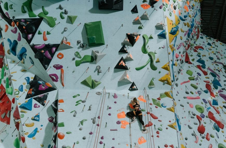Striking indoor climbing gym featuring a textured, multi-colored wall covered in a diverse assortment of climbing grips and protrusions.