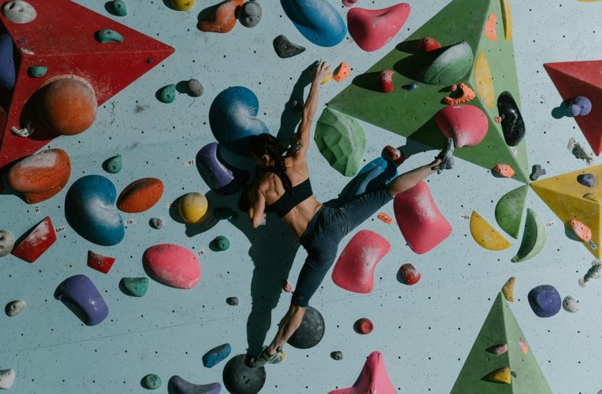 An athlete in black climbing gear gripping onto diverse-shaped artificial rock formations on a wall, showcasing the skill and athleticism required for indoor rock climbing.