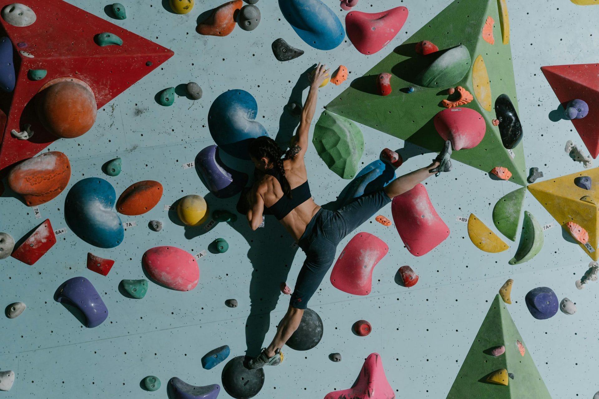 An athlete in black climbing gear gripping onto diverse-shaped artificial rock formations on a wall, showcasing the skill and athleticism required for indoor rock climbing.