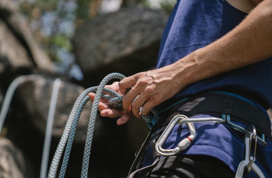 Close-up view of a climber's hands fastening carabiners and securing a climbing rope, highlighting the attention to safety and equipment necessary for challenging activities.